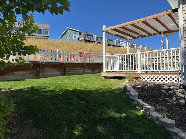 Expansive lawn, multi-level retaining walls, concrete paver landscaping, wood deck with white railing, and a covered patio structure