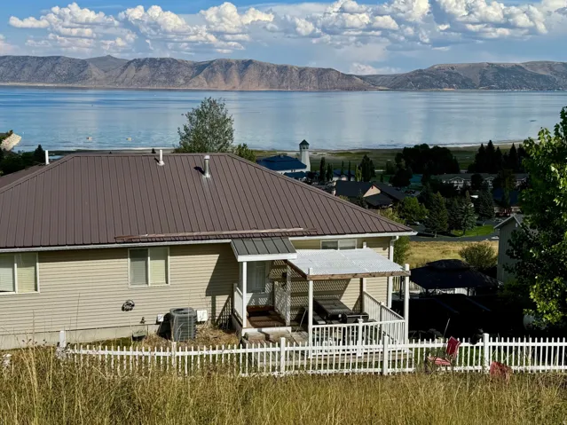 Metal roof, horizontal siding, covered porch, white picket fence, mountain and water backdrop