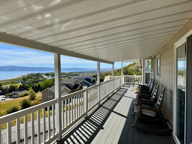 Expansive covered deck featuring a lake and mountain backdrop, durable composite decking, white railing, and sliding glass door access