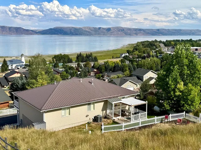 Aerial perspective featuring a metal roof, covered patio, white picket fence, and distant body of water