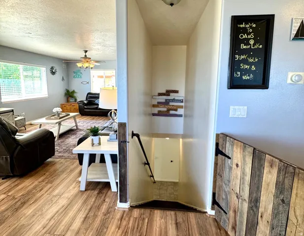 Wood-finish flooring throughout the main living area, a ceiling fan with integrated lighting, and a window with horizontal blinds