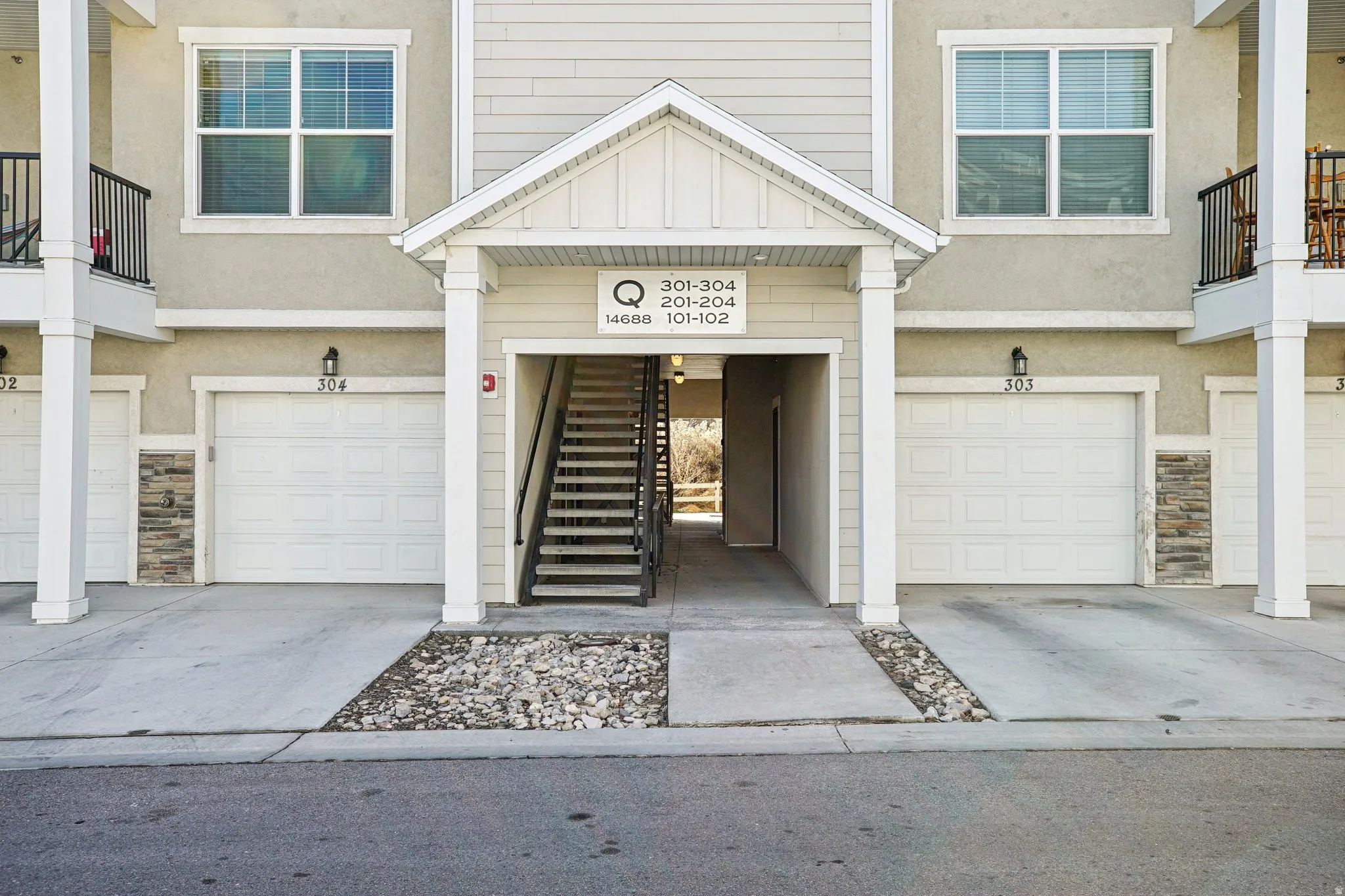 Multi-unit exterior with individual garage entrances featuring light stucco siding and stacked stone accents