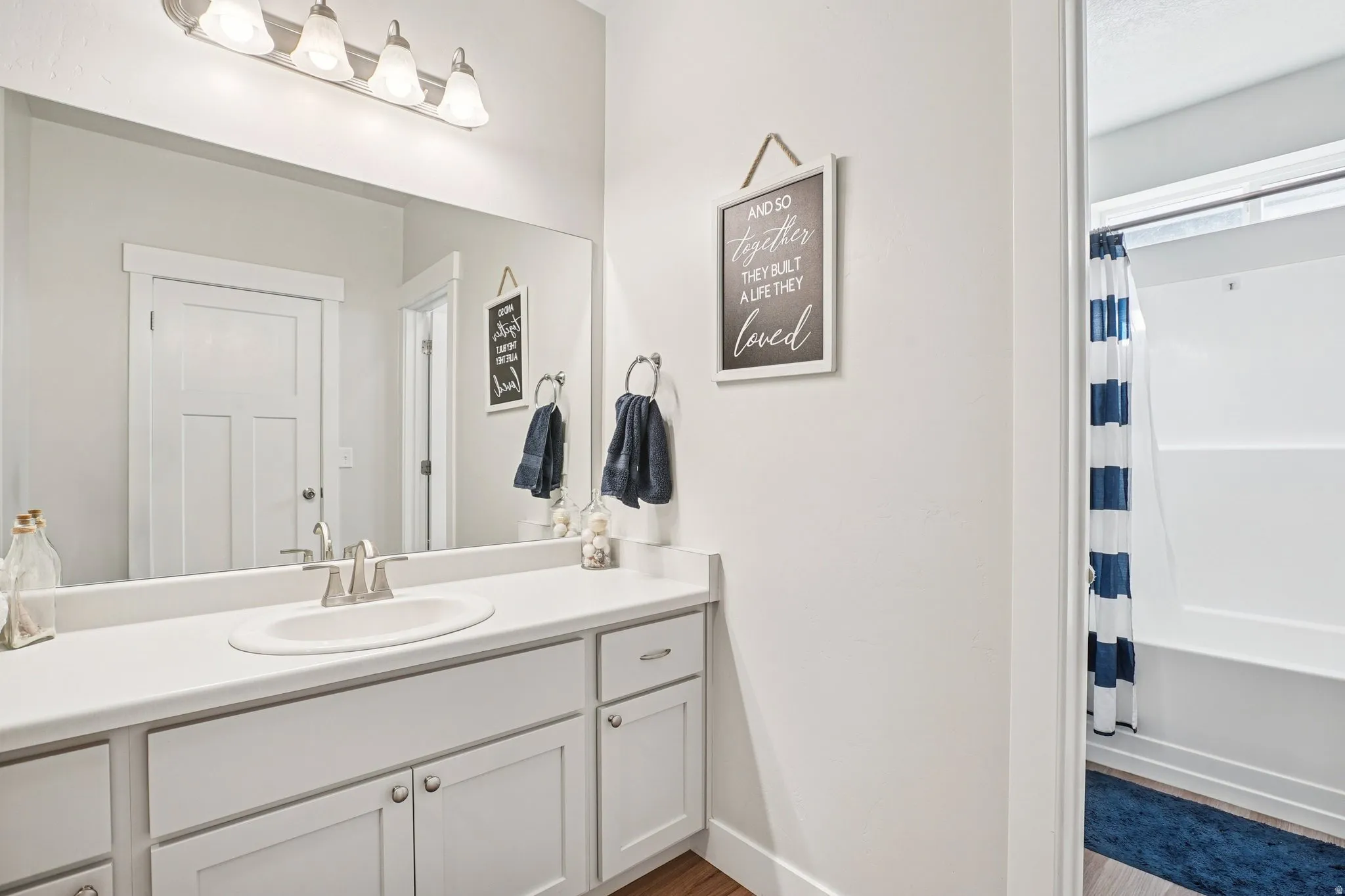 White vanity with a built-in sink, brushed nickel faucet, large wall mirror, and a four-light fixture
