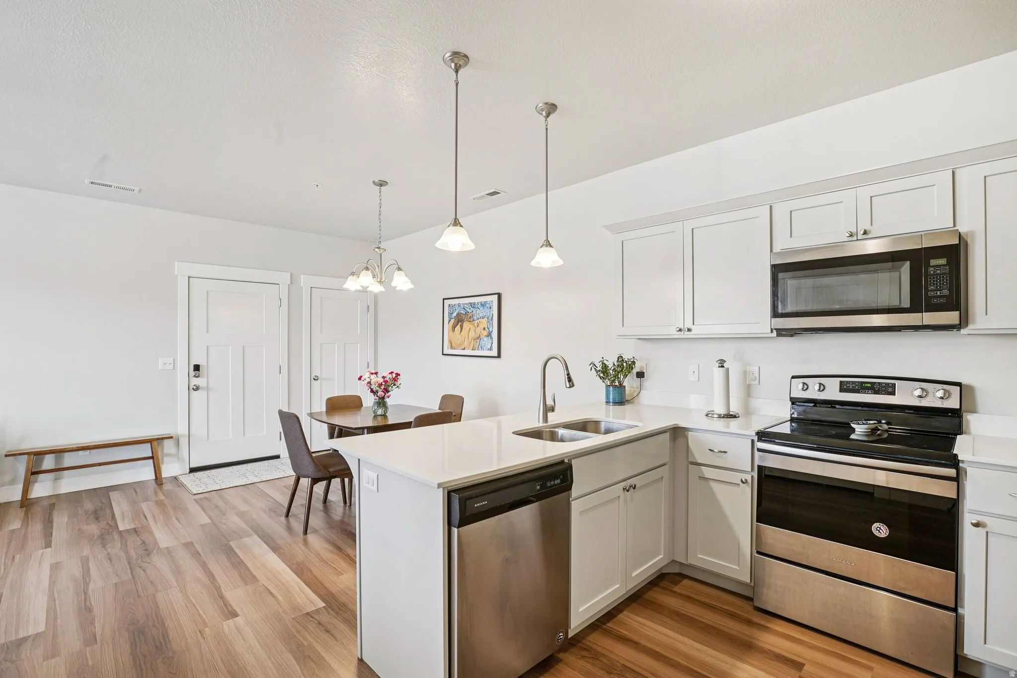 White shaker cabinetry with crown molding, stainless steel appliances, wood-finish flooring, white quartz countertops, and a double basin sink