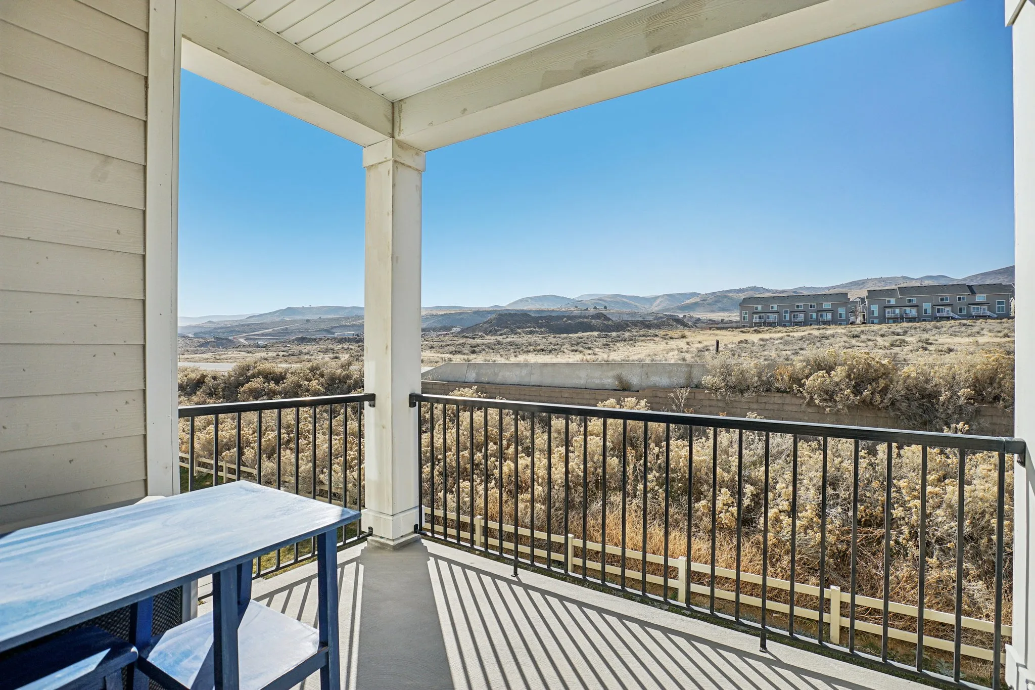 Covered balcony with white siding, black metal railing, and distant mountain scenery
