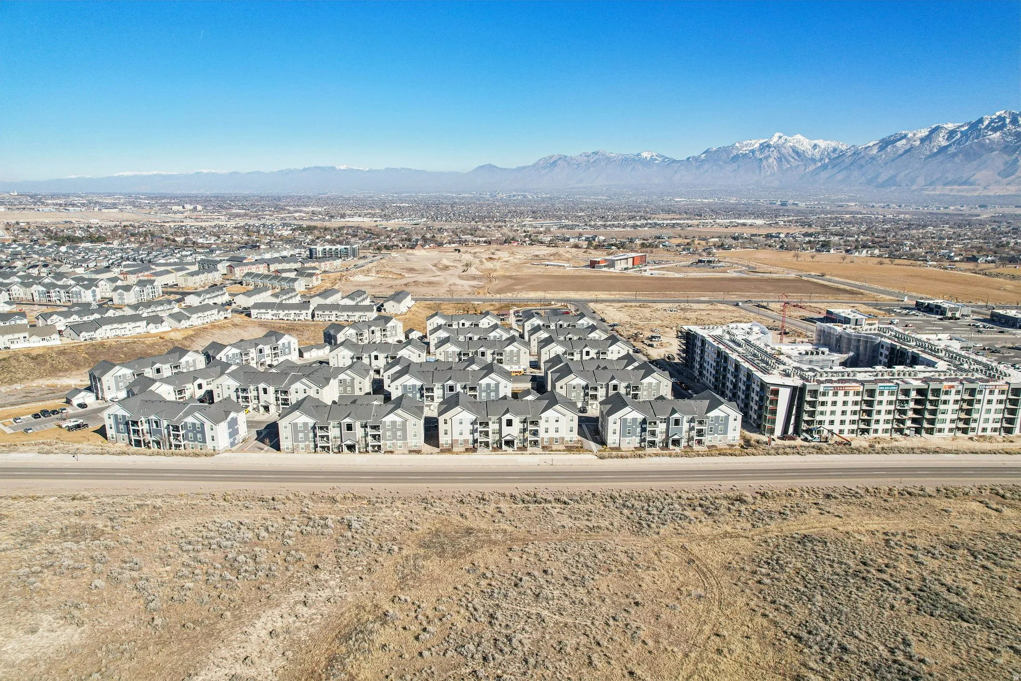 Expansive aerial perspective showcasing a residential development with multiple apartment complexes, several multi-story buildings, and a distant mountain range