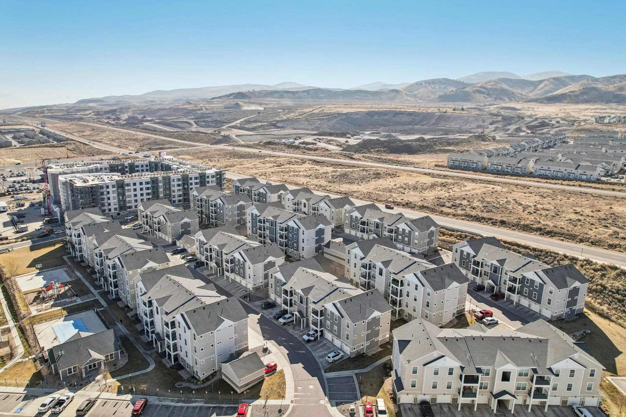 Expansive residential community featuring multi-story buildings with balconies, paved parking areas, and a visible playground