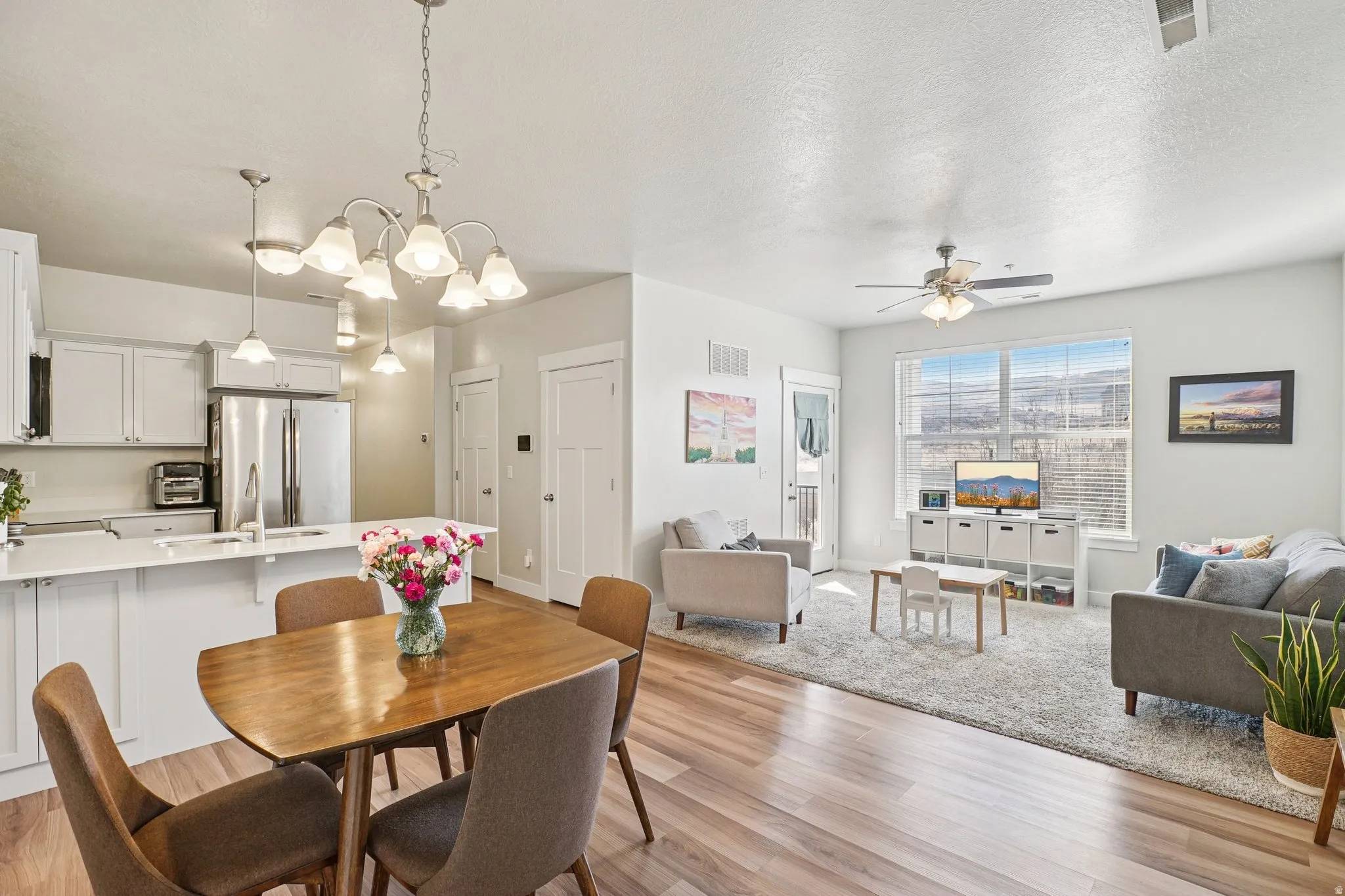Spacious open-concept living area with wood-finish flooring, white cabinetry, a built-in kitchen island, and stainless steel appliances