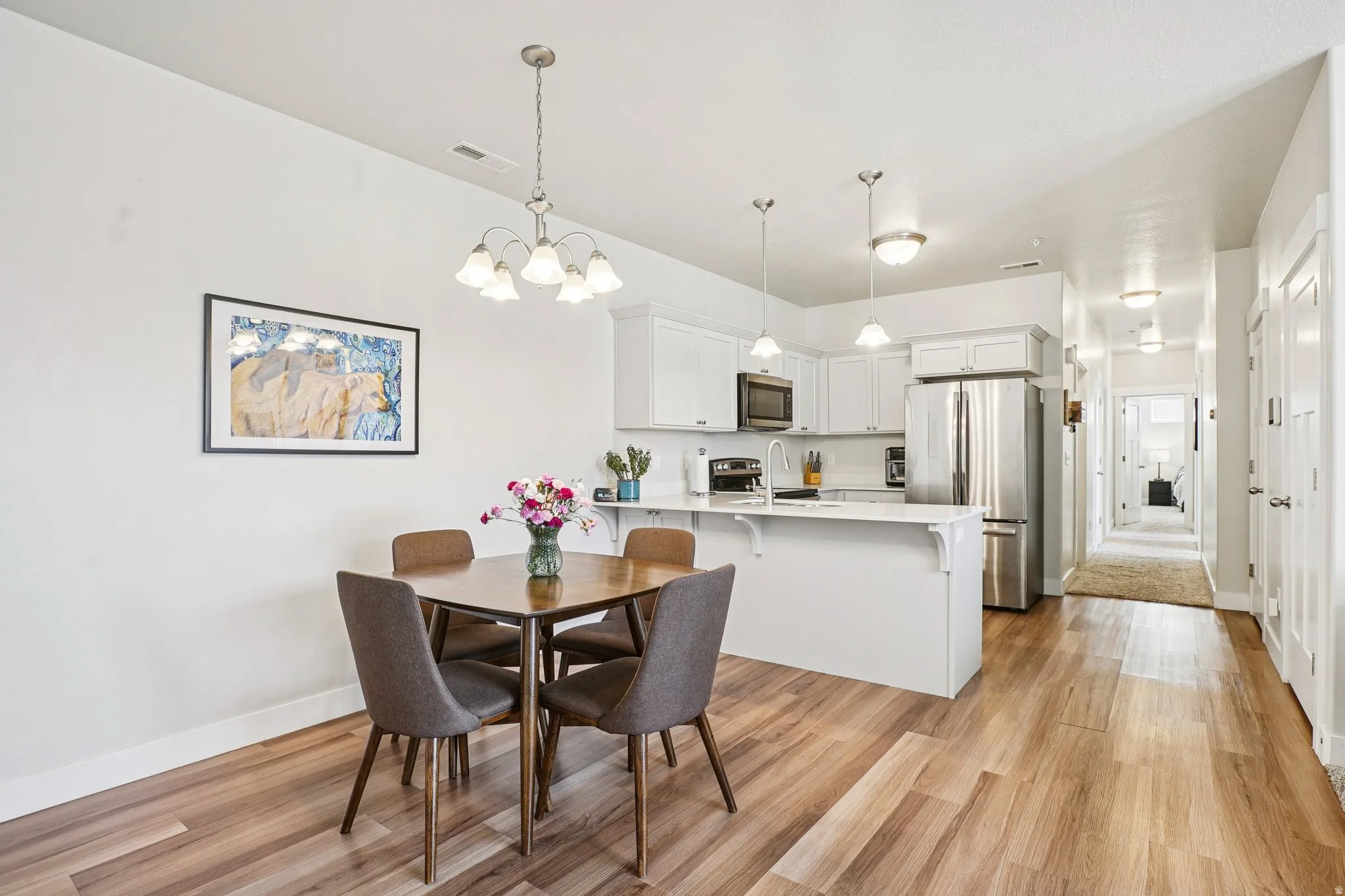 Open-concept kitchen and dining area featuring wood-finish flooring, white cabinetry, stainless steel appliances, and a kitchen island with pendant lighting