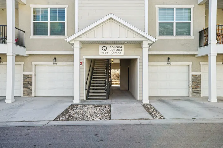 Multi-unit exterior with individual garage entrances featuring light stucco siding and stacked stone accents
