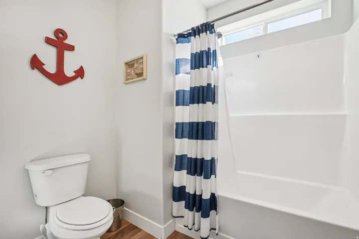 White toilet with a built-in tank, a white tub and shower combination, and wood-finish flooring
