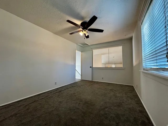 Room featuring textured ceiling, ceiling fan with light fixture, carpeted flooring, and window with blinds