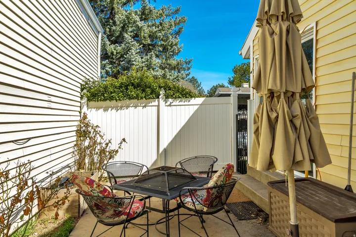 Paved patio area, white horizontal siding, white privacy fence, mature trees, and shrubs