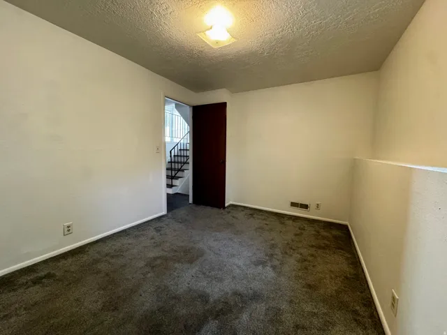 Carpeted flooring, white painted walls, and a staircase with dark handrails