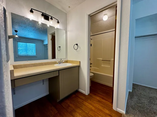 Wood-finish flooring, vanity with integrated sink, overhead track lighting, and a full-width mirror