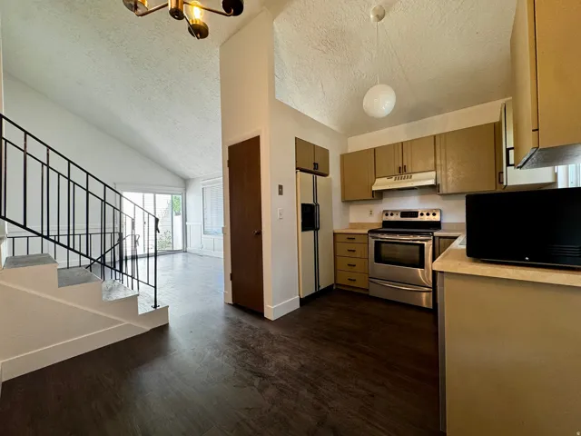 Vaulted ceiling, open staircase with metal railing, wood-finish flooring, full-size refrigerator, and stainless steel range
