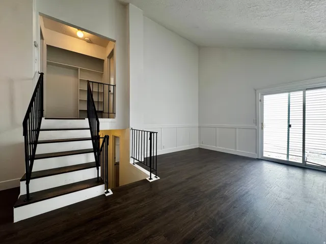 Vaulted ceiling with dark wood-finish flooring, white paneling, and a sliding glass door