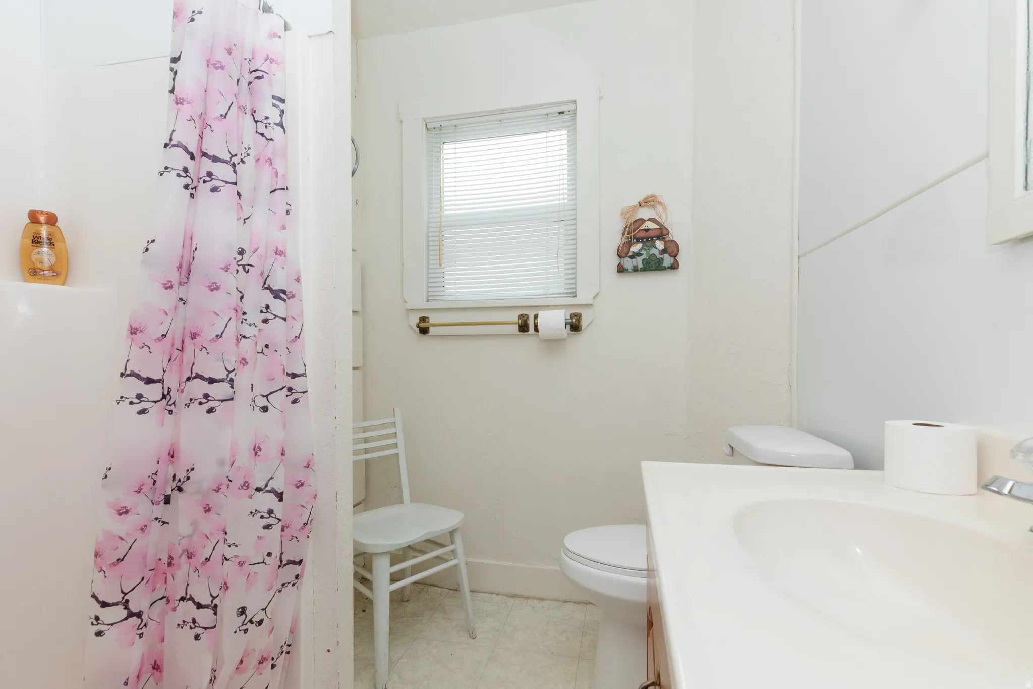 Bathroom featuring a single vanity, built-in tub with shower, and window with blinds