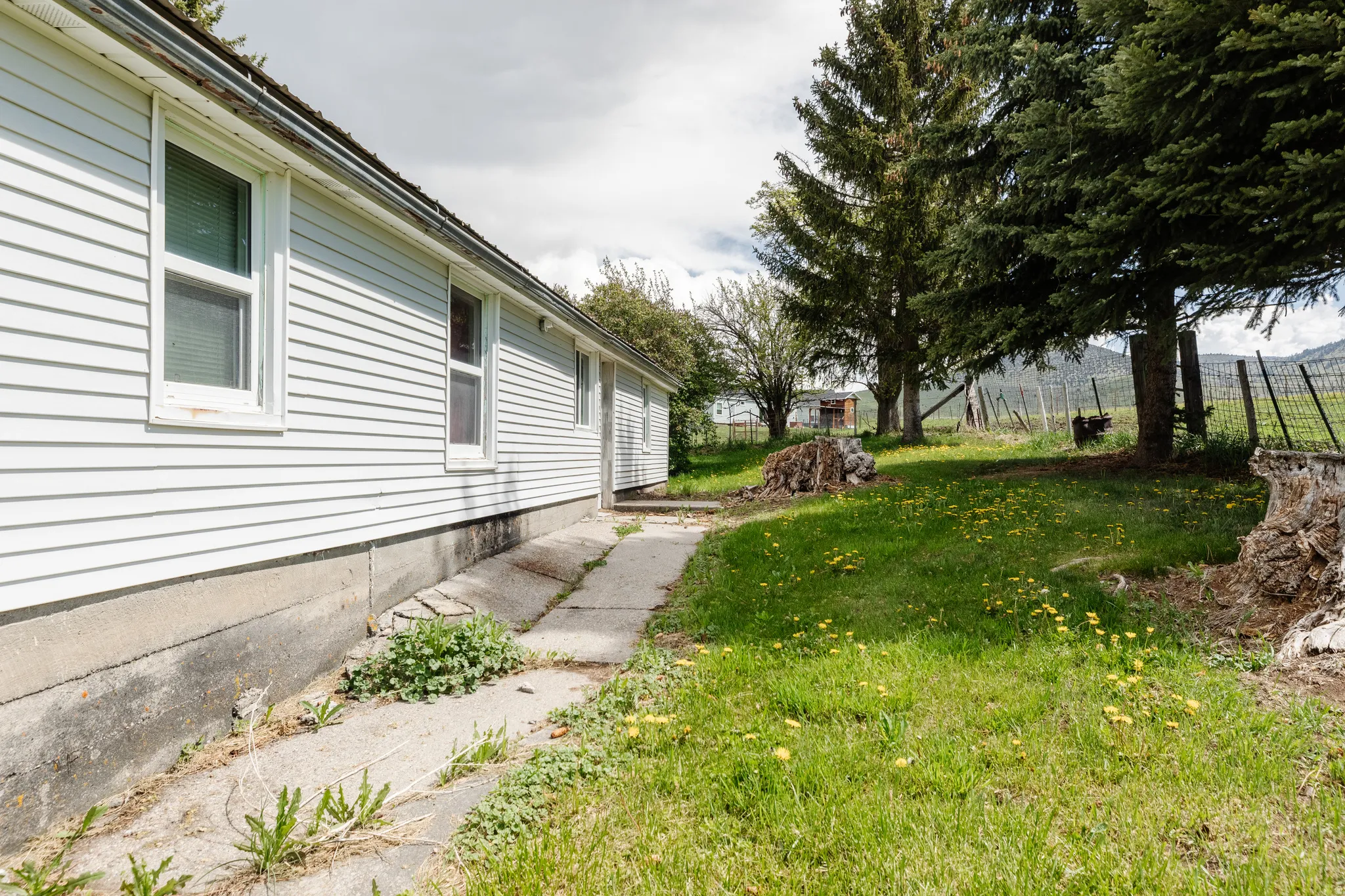 White siding exterior with multiple windows, concrete foundation, and a concrete pathway
