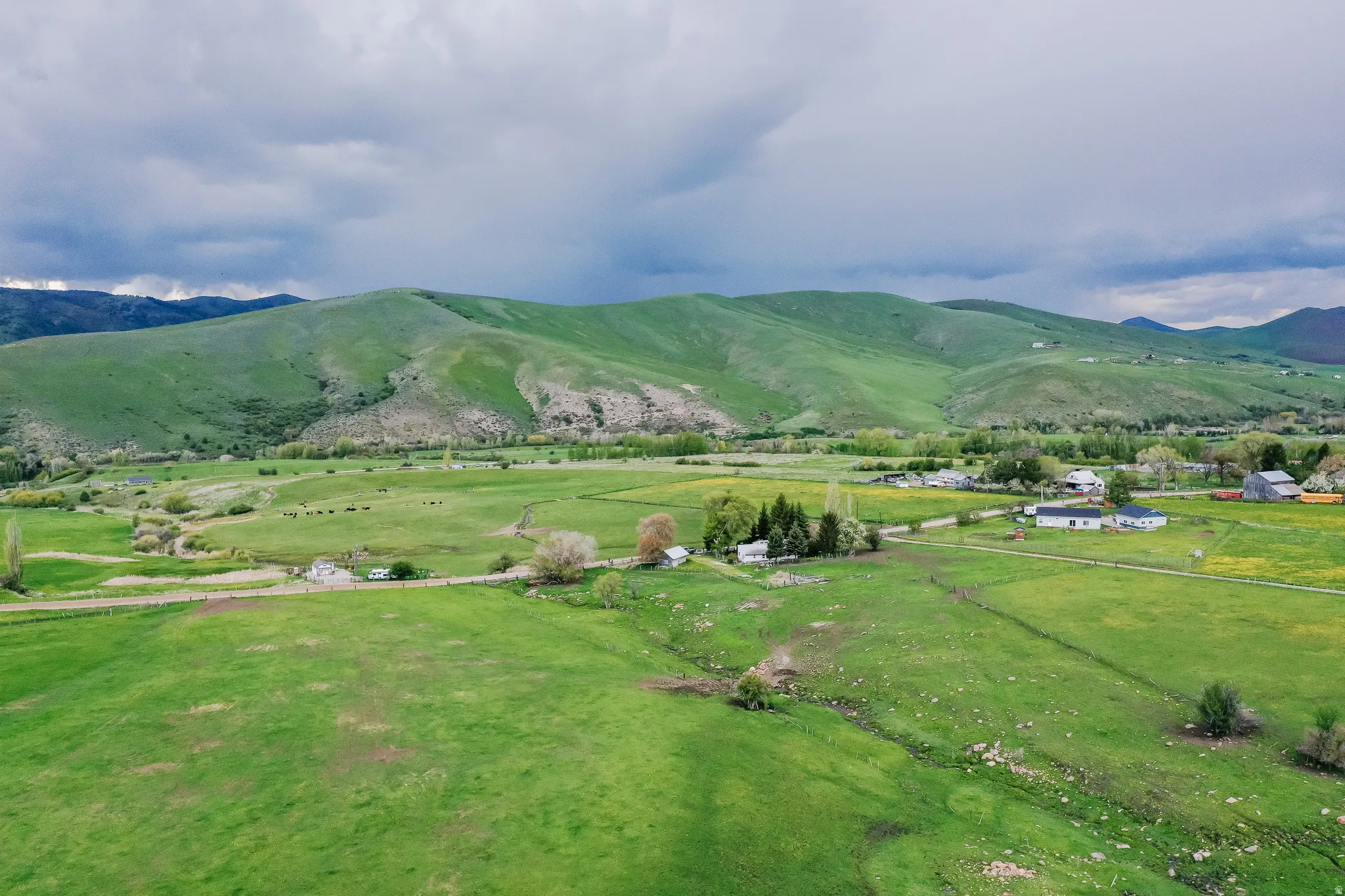 Expansive green fields with rolling hills, scattered structures, distant mountains, and a clear sky
