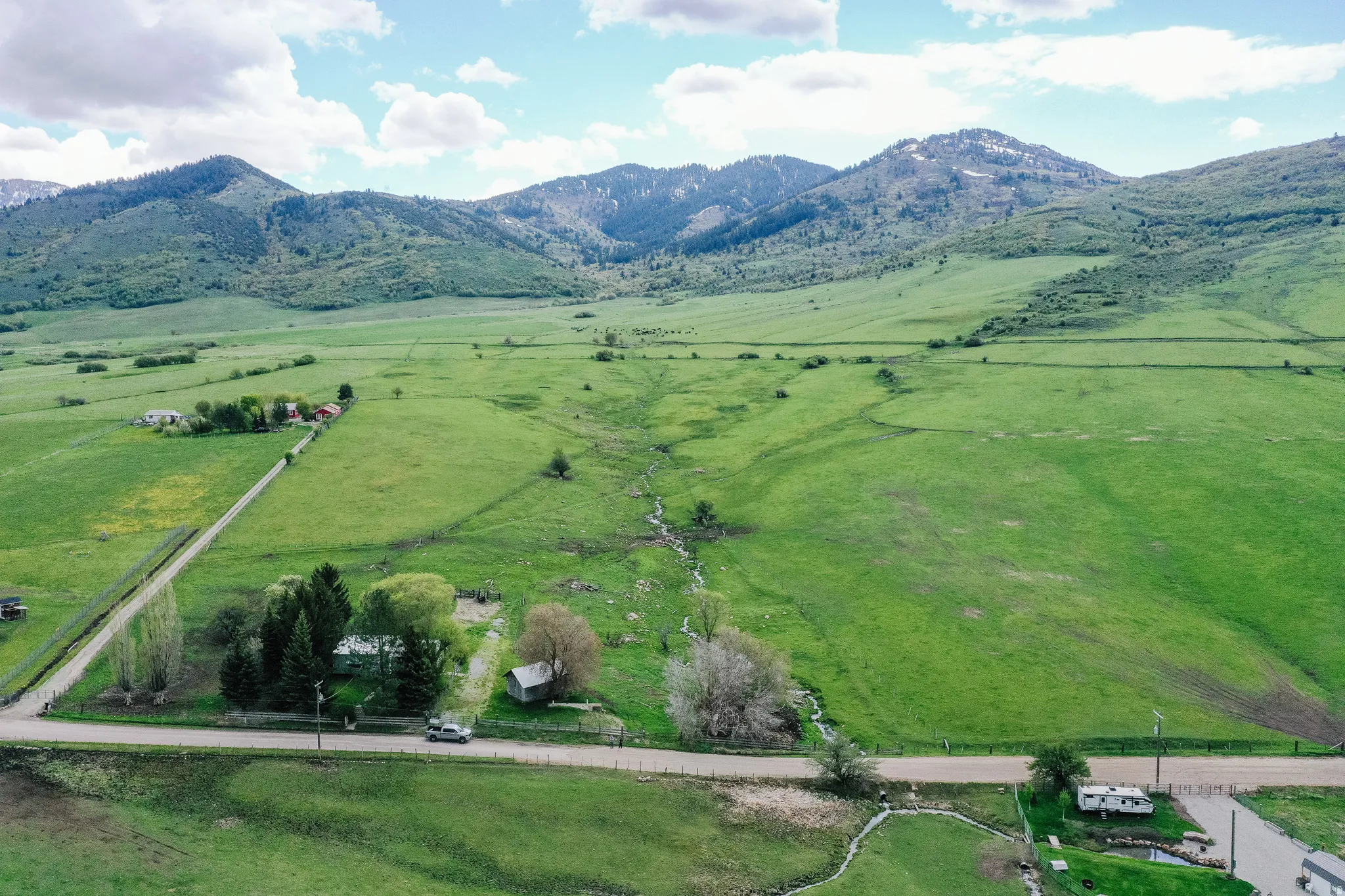 Expansive green acreage with distant mountains, a meandering stream, and a rural road