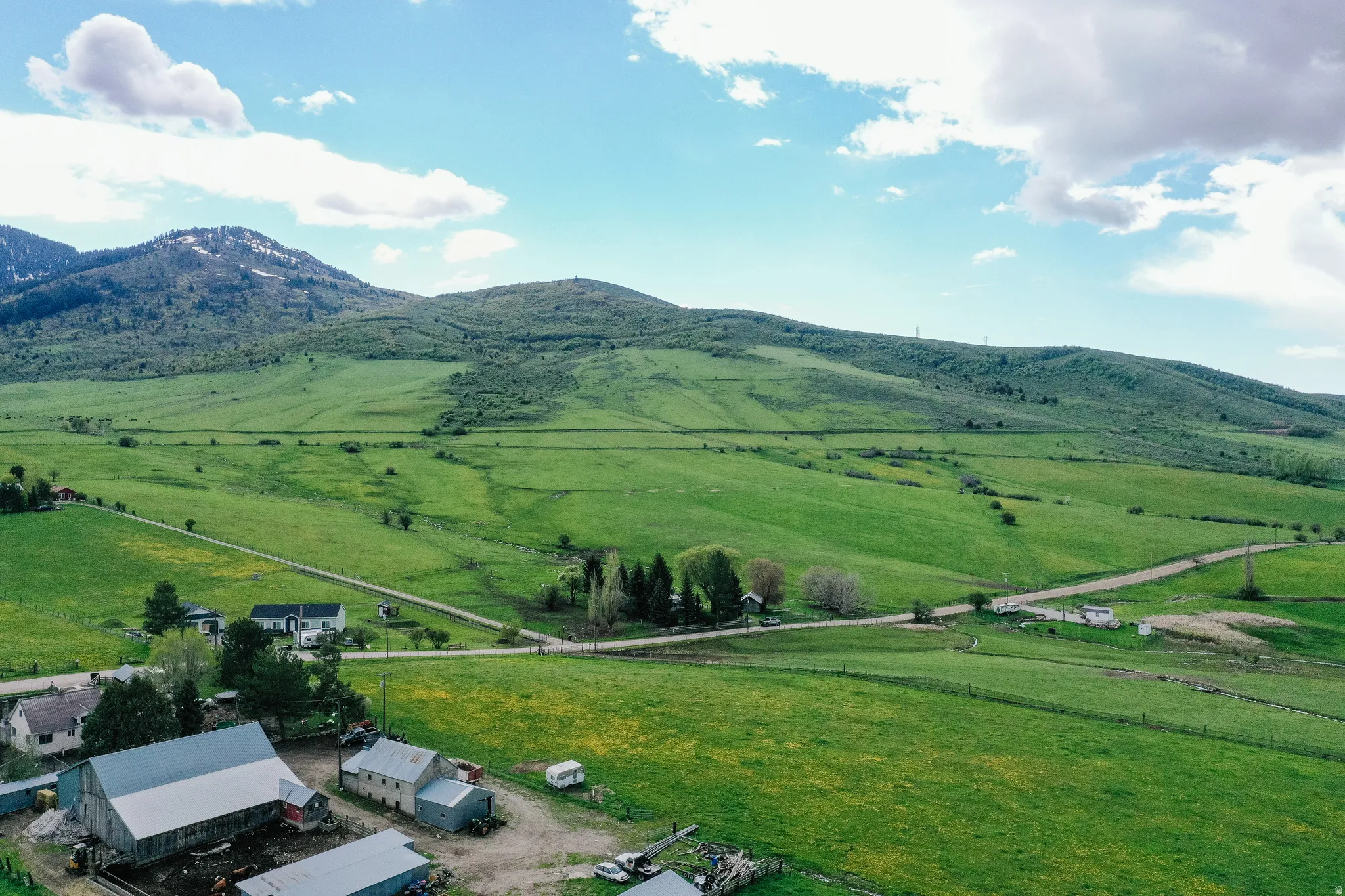 Expansive green landscape with distant mountains, multiple outbuildings, and a single-story residence