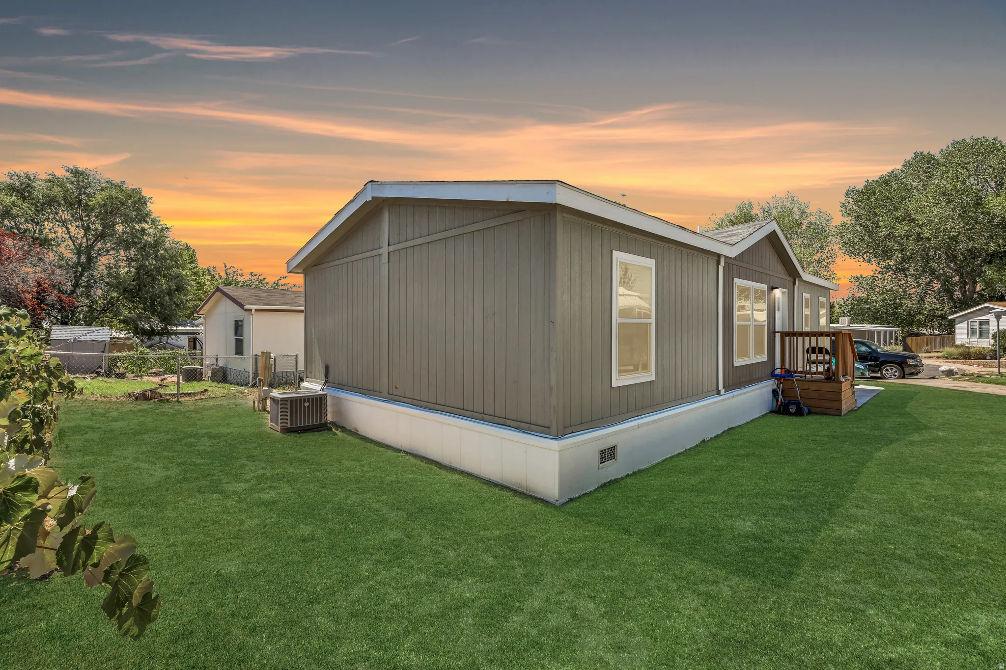 Exterior featuring vertical panel siding, multiple windows, a small wooden deck, and a green lawn