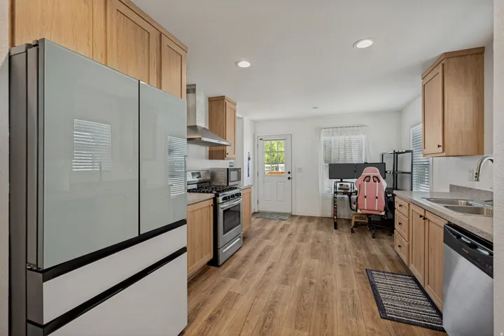 Kitchen featuring wood-finish flooring, light wood cabinetry, stainless steel appliances, and a double-basin sink