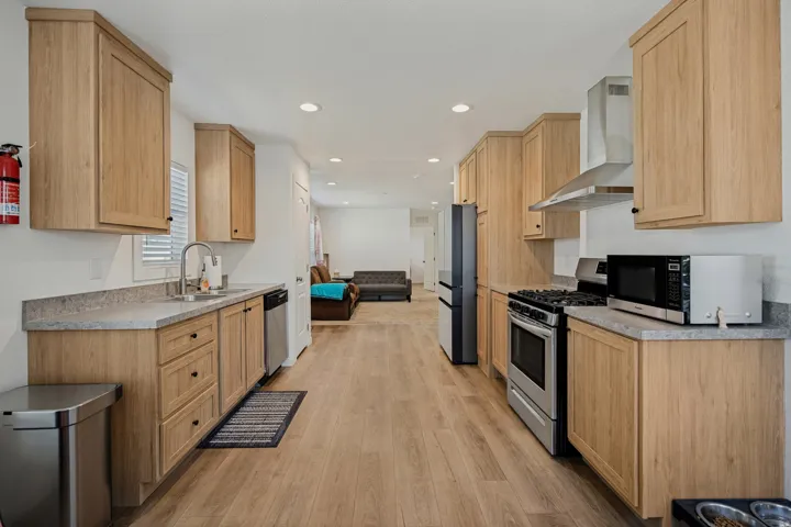 Kitchen featuring wood-finish cabinetry, stainless steel appliances, light-toned countertops, wood-finish flooring, and recessed lighting