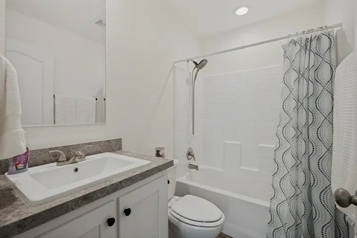 White vanity with dark hardware, undermount sink, and stone-finish countertop