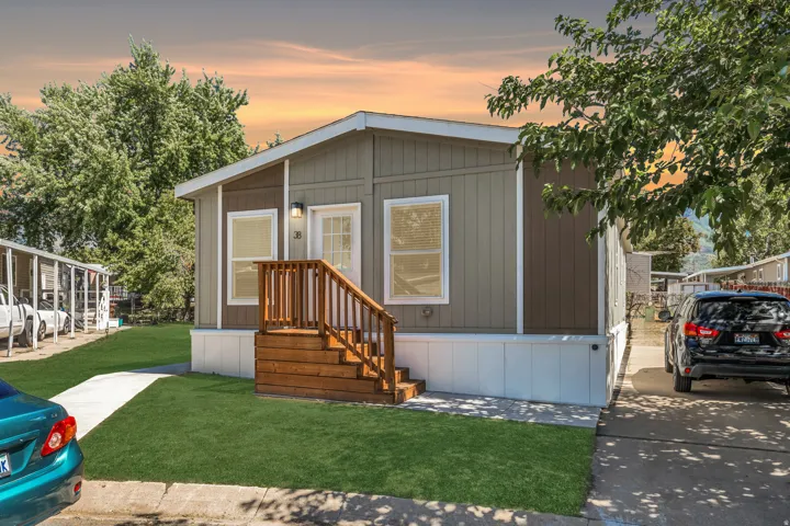 Exterior featuring a wooden entry staircase, a concrete driveway, a concrete walkway, and a landscaped lawn