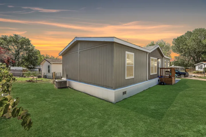 Exterior featuring vertical panel siding, multiple windows, a small wooden deck, and a green lawn