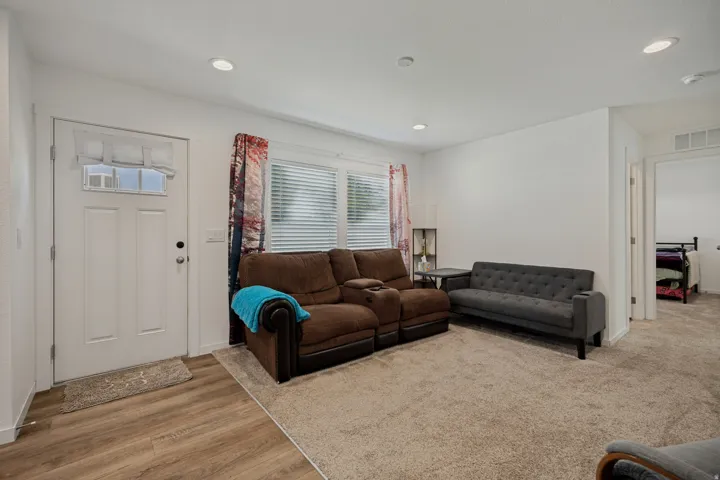 Laminate wood-finish flooring, recessed lighting, white walls, and a white entry door with a privacy window