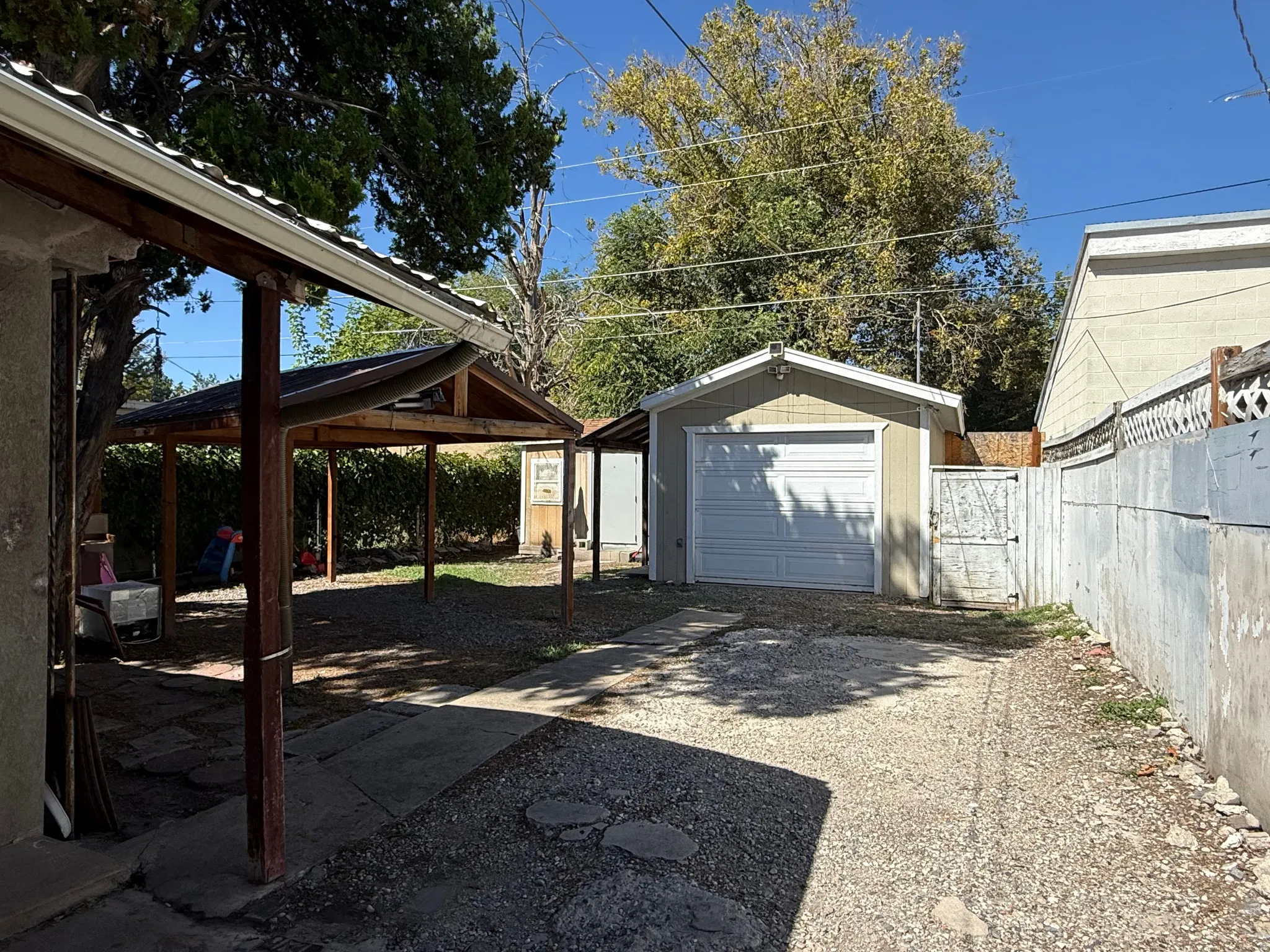 Detached garage with a roll-up door, covered patio structure, side yard access, and a gravel driveway
