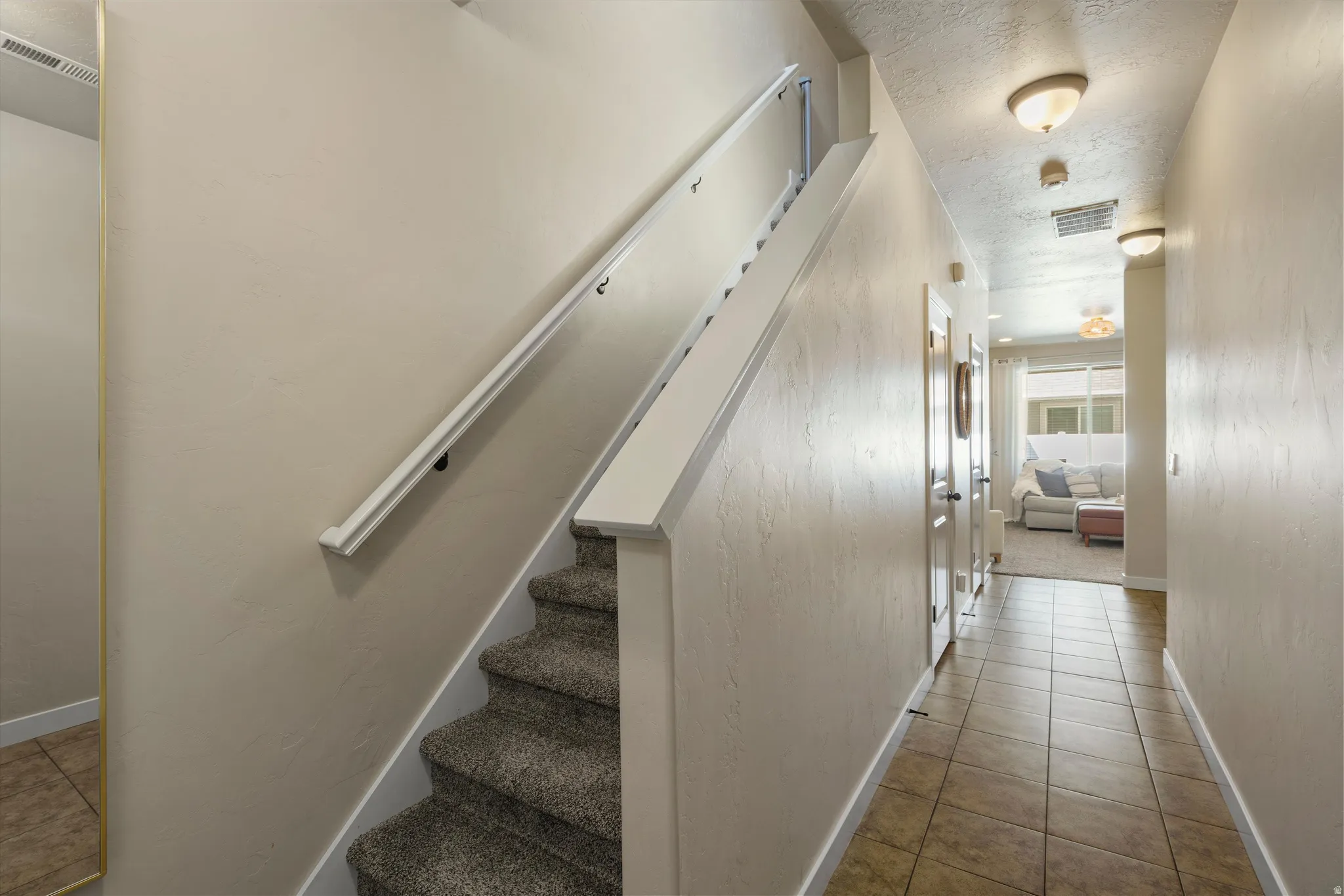 Staircase with carpeted treads and white handrail, complemented by a tiled hallway with flush-mount lighting