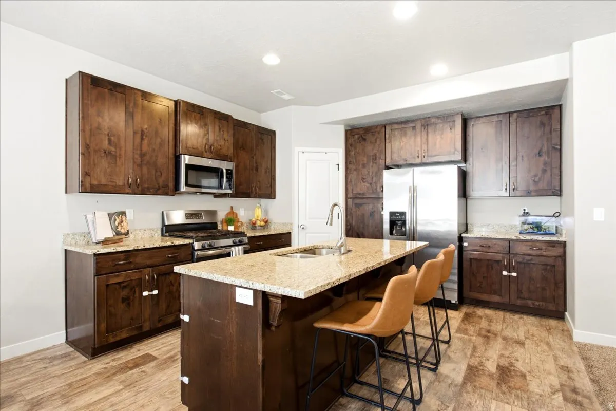 Dark wood-finish cabinetry, granite countertops, stainless steel appliances, wood-finish flooring, and recessed lighting