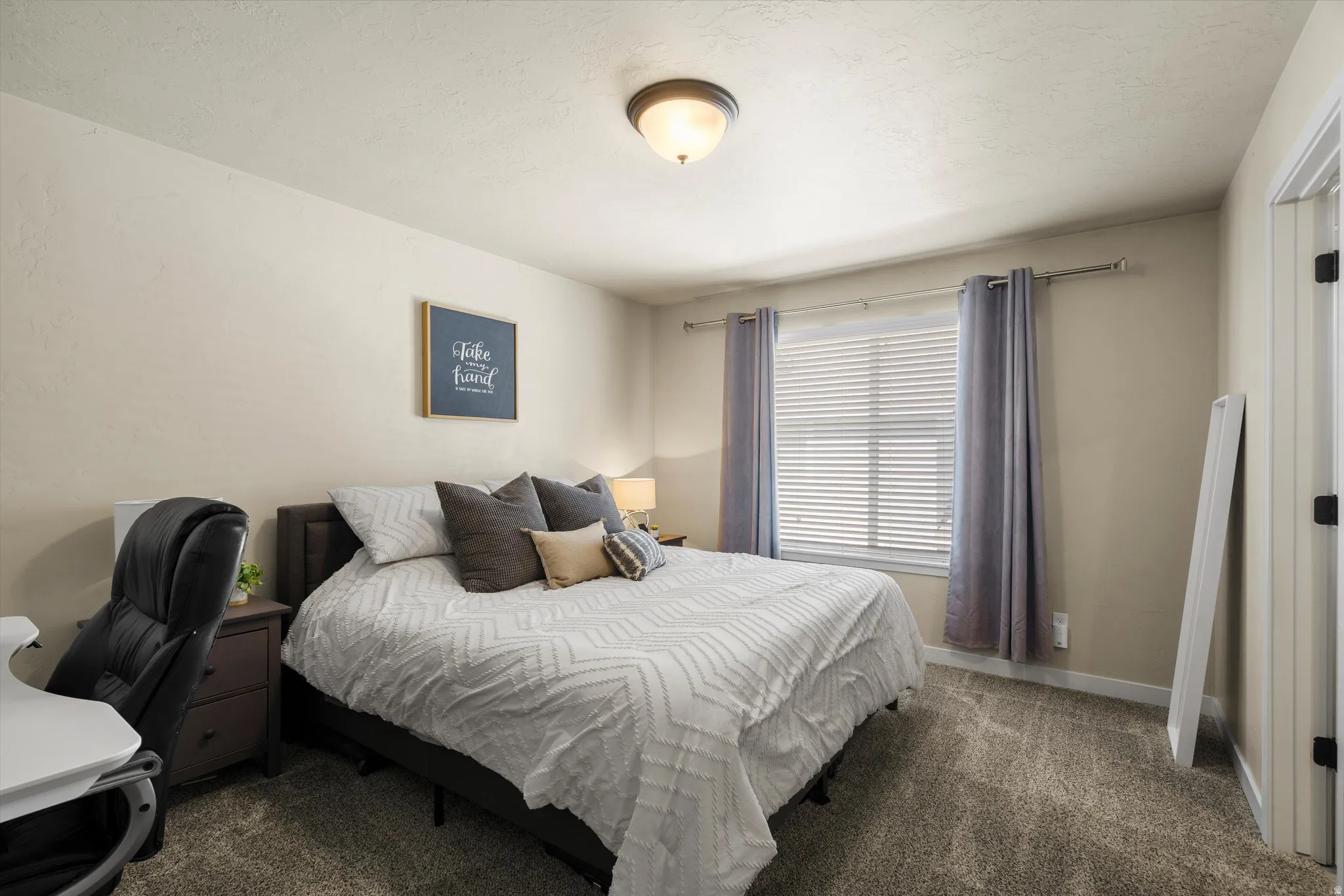 Textured carpeting throughout, featuring a single window with blinds and curtains