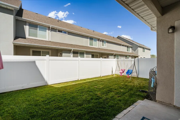 Fenced backyard with a manicured lawn, concrete patio, and exterior wall light fixture