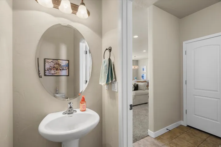 Pedestal sink with chrome faucet, oval mirror, and three-light vanity fixture
