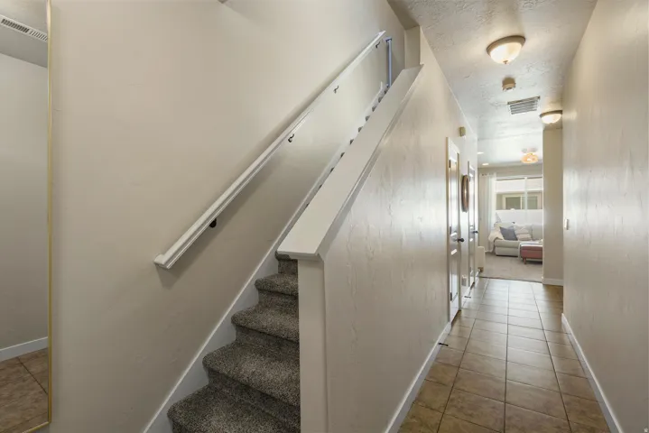 Staircase with carpeted treads and white handrail, complemented by a tiled hallway with flush-mount lighting