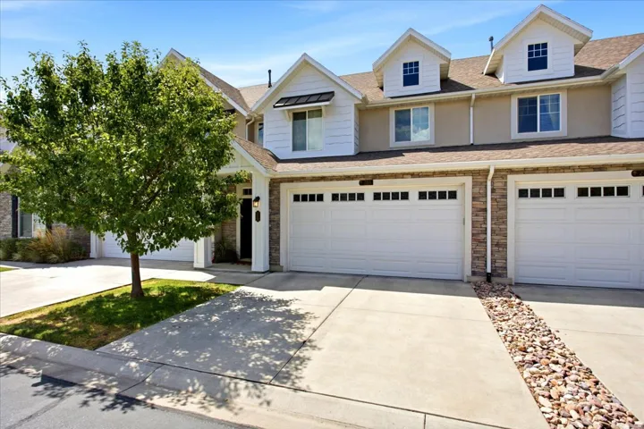 Contemporary townhouse exterior featuring white siding, stone veneer accents, and multiple dormer windows