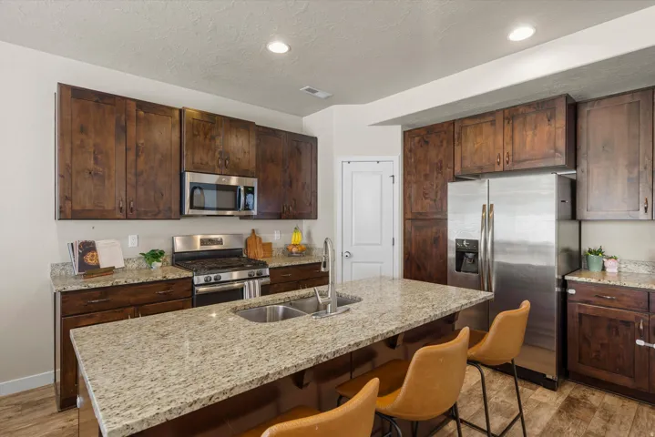 Kitchen featuring wood-finish cabinetry, stainless steel appliances, a kitchen island with a double basin sink, and granite countertops