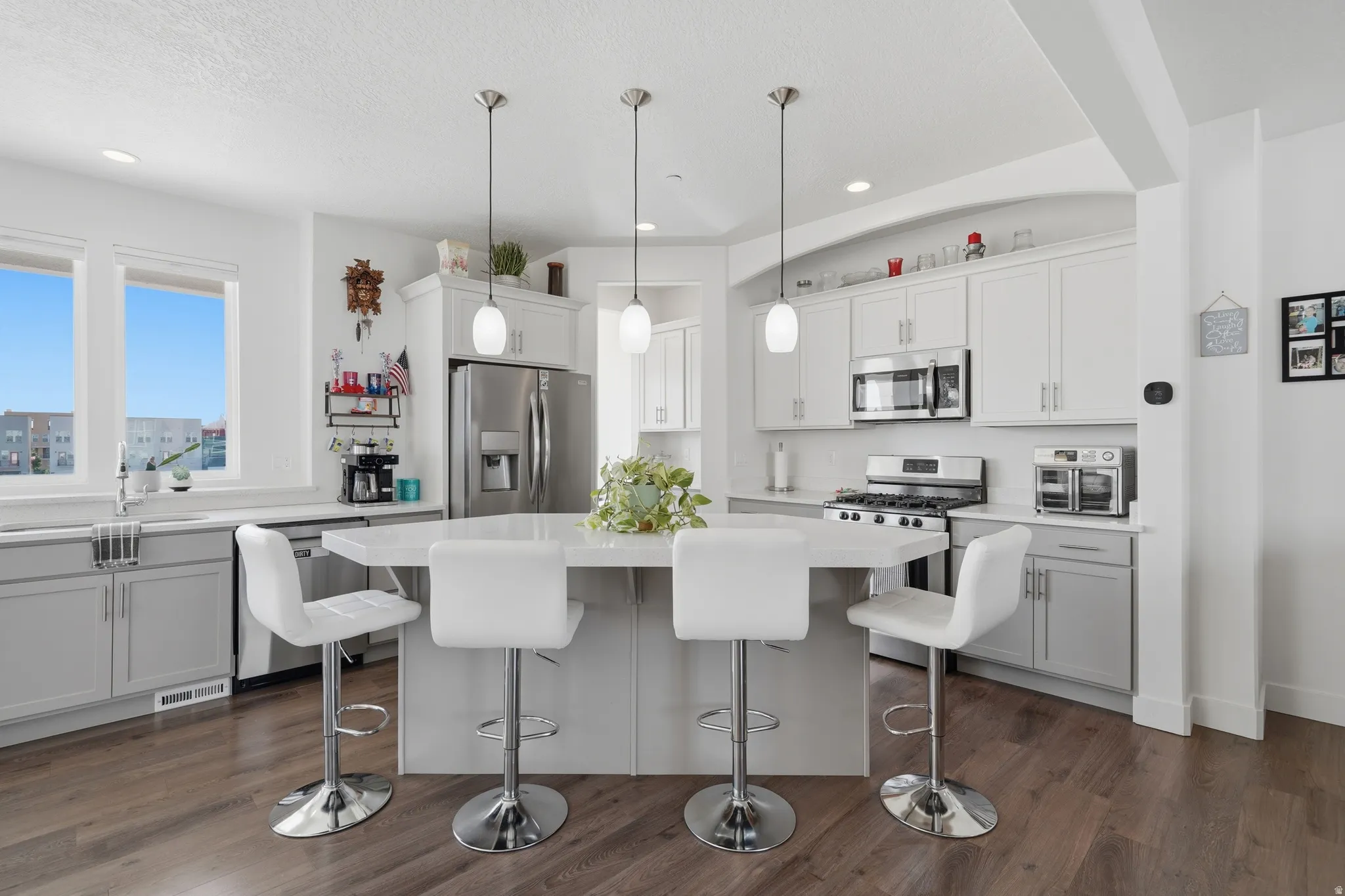 Kitchen featuring a central island with pendant lighting, stainless steel appliances, dual-tone cabinetry, and wood-finish flooring
