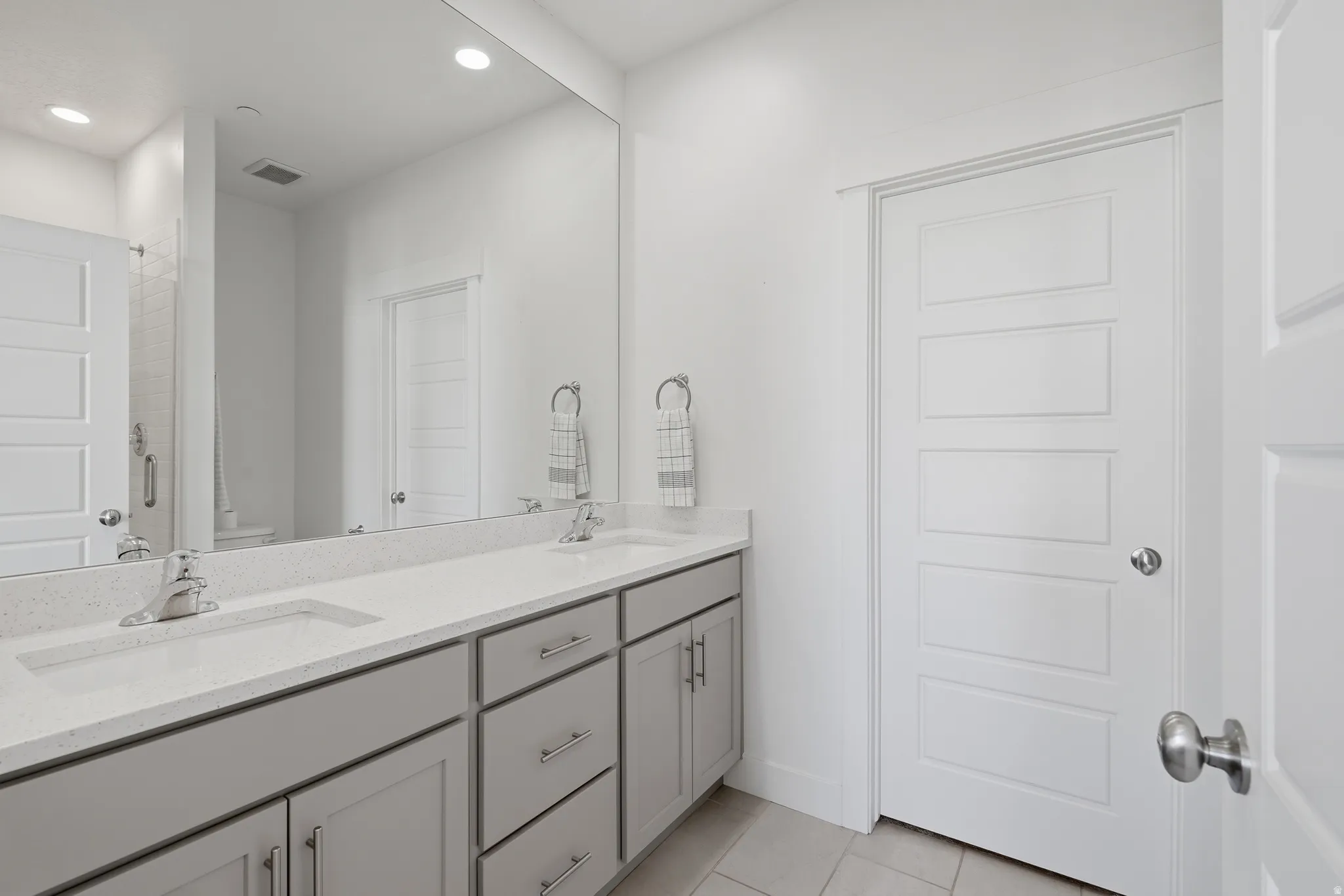 Dual vanity with integrated sinks, quartz countertop, gray shaker cabinetry, and polished chrome fixtures