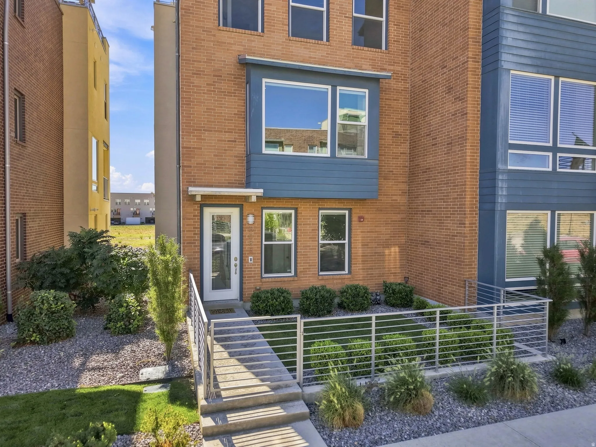 Brick exterior with blue paneling, multiple windows, metal railings, and landscaping
