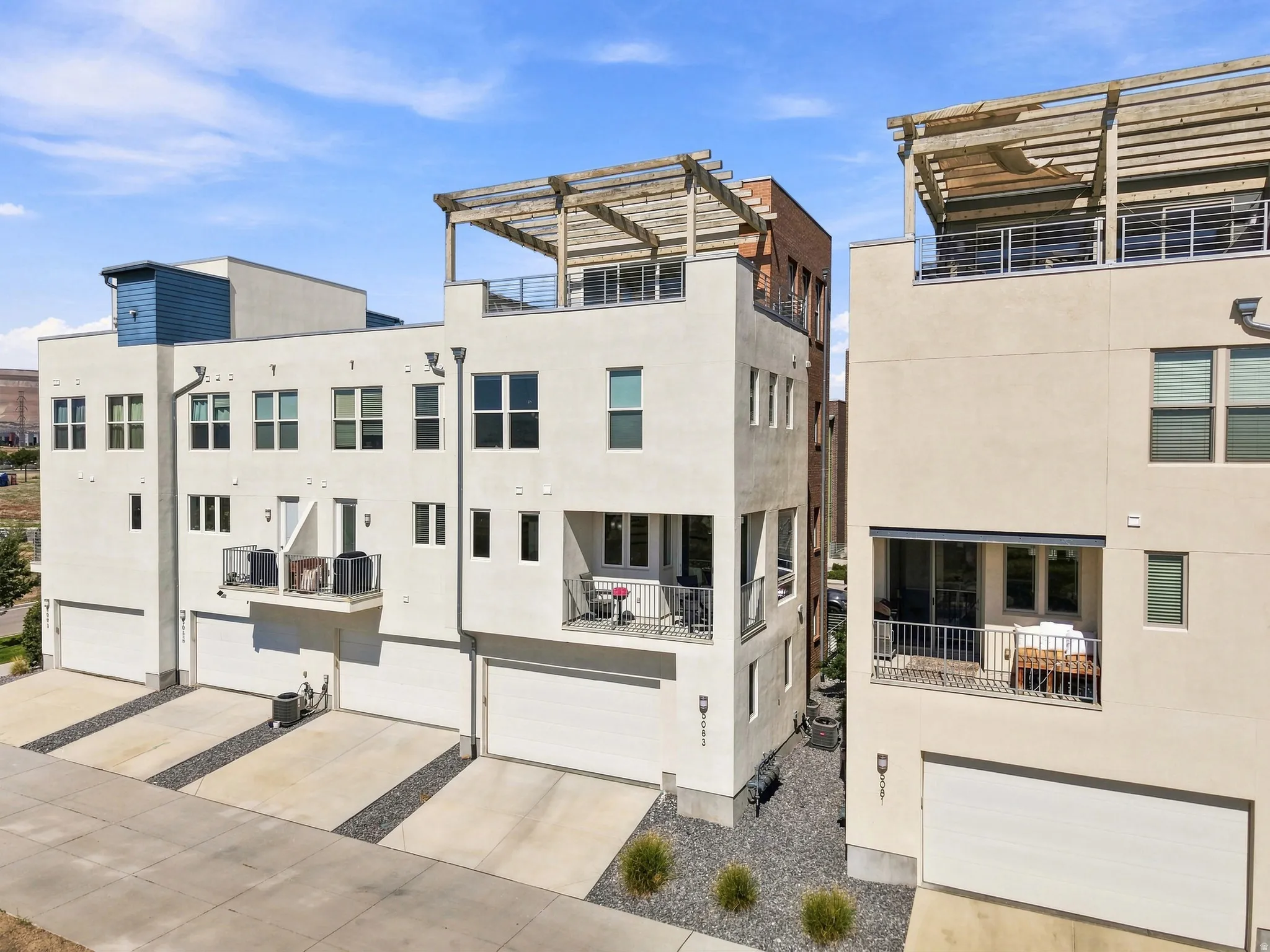 Contemporary multi-story exterior with integrated garages, private balconies, and rooftop deck with a pergola