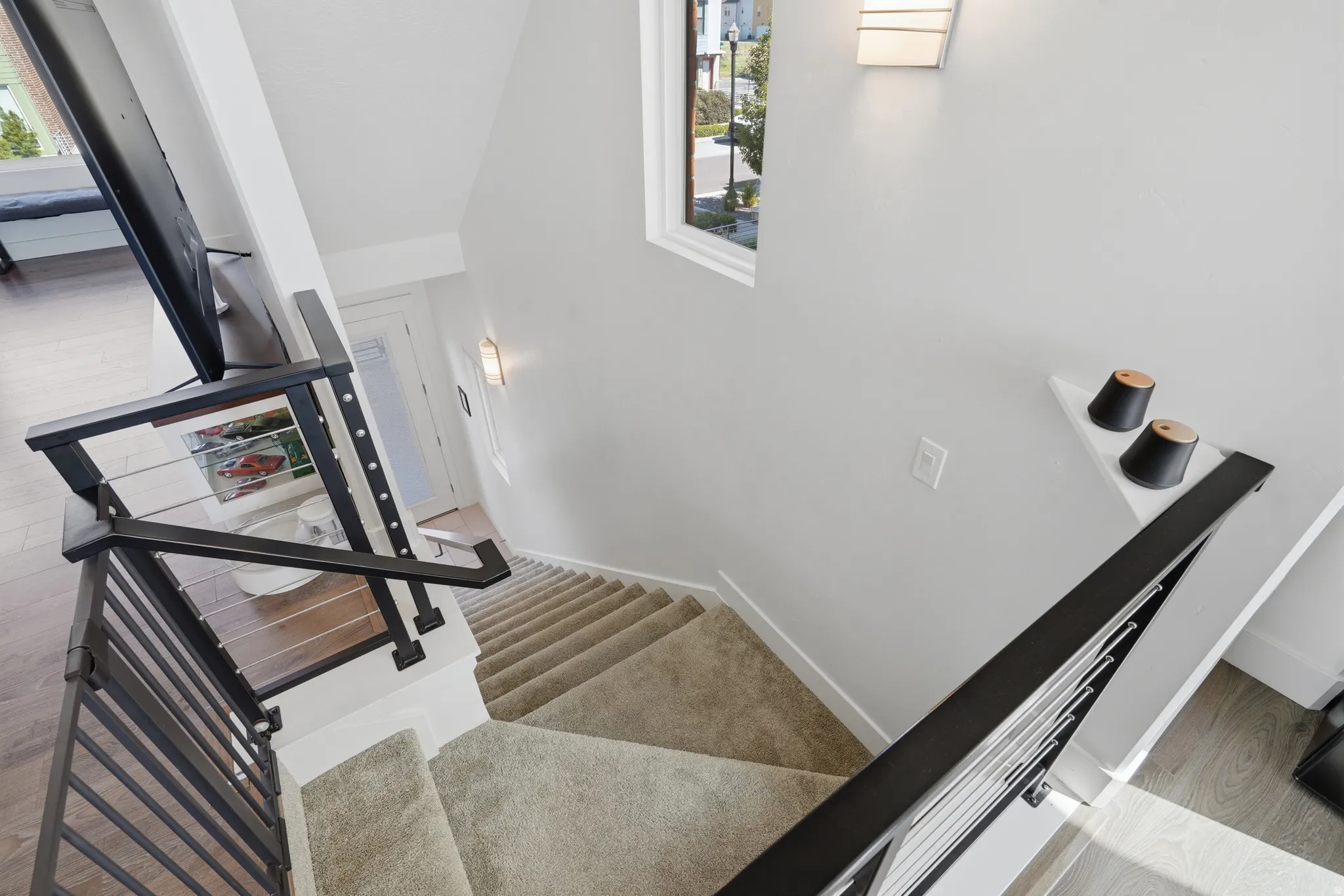 Modern black metal stair railing with cable infill, white walls, carpeted stairs, and wood-finish flooring