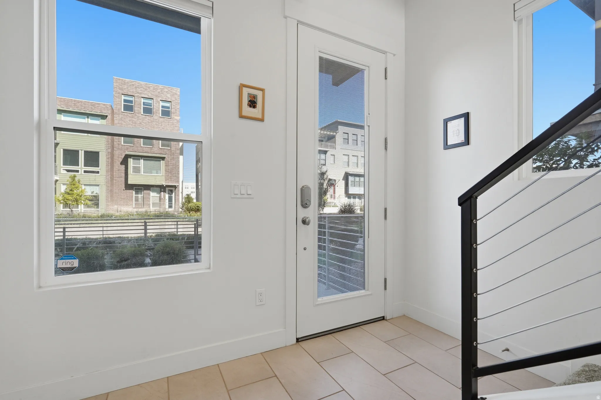 White interior walls, light-toned tile flooring, modern white door with full-light panel, contemporary metal and cable stair railing, double-hung window
