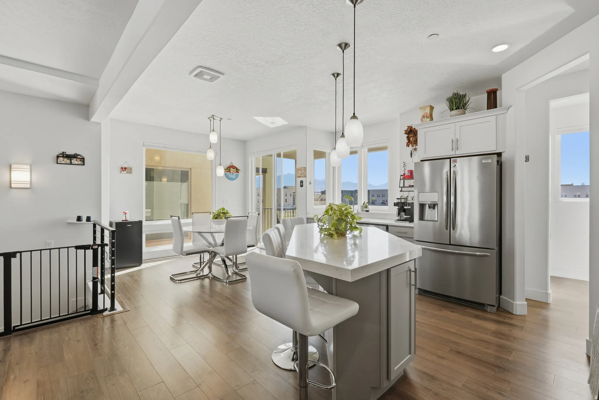 Open-concept kitchen and dining area featuring wood-finish flooring, a kitchen island with pendant lighting, stainless steel appliances, and white cabinetry