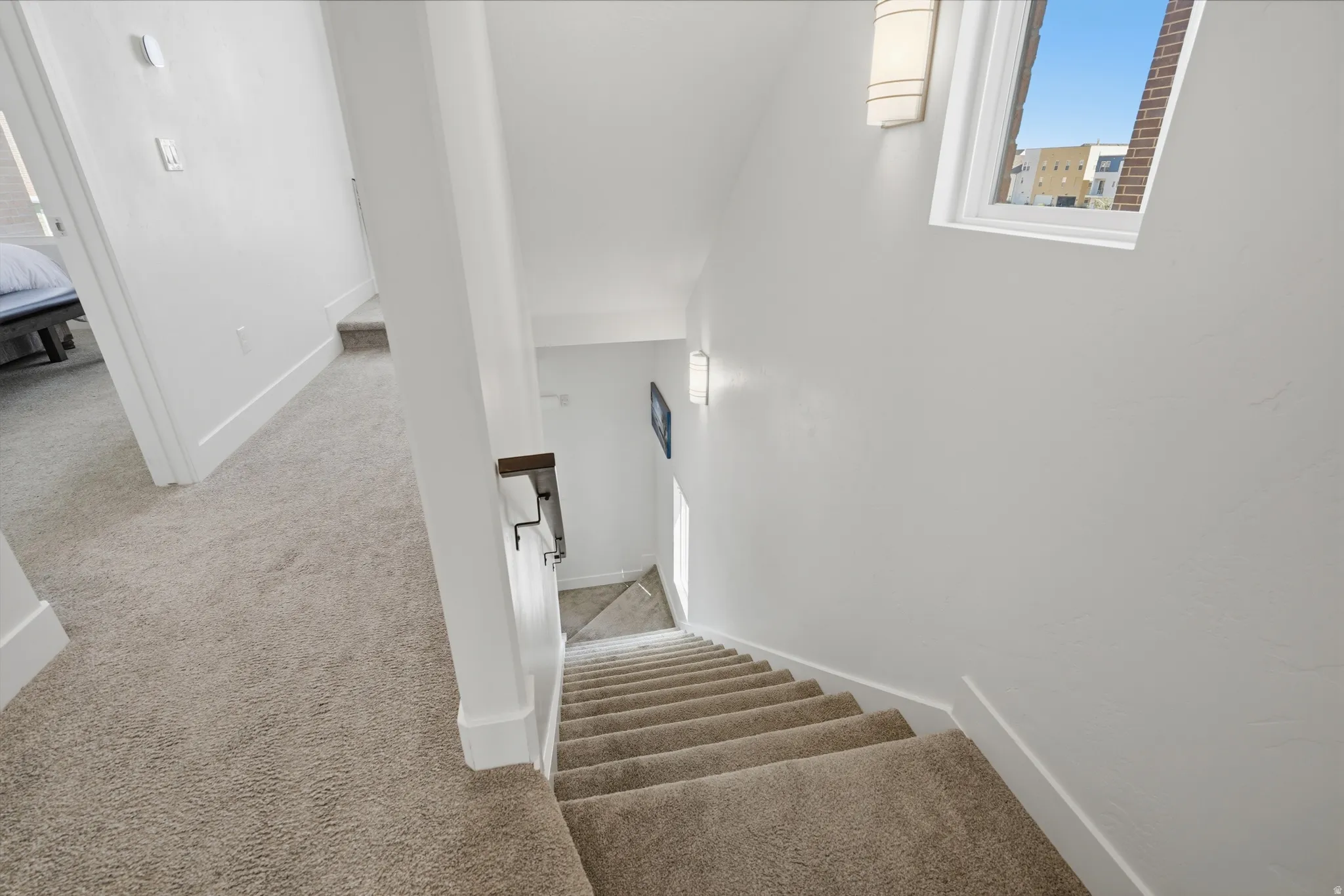 Carpeted staircase with white walls, a single window, and wall-mounted sconce lighting